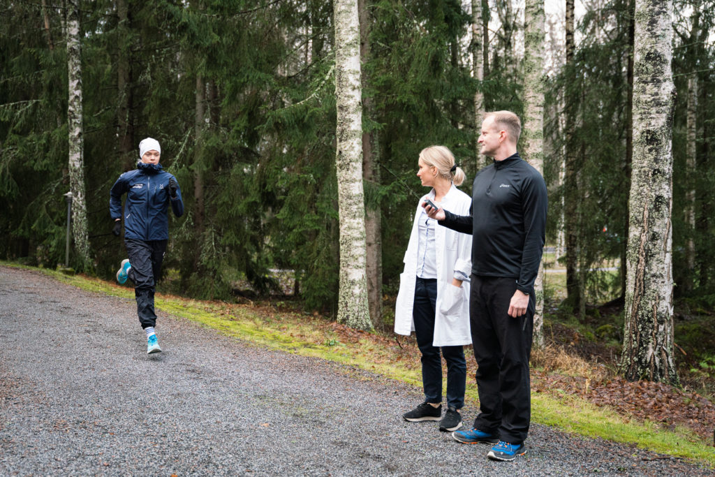 Tampereen urheilulääkäriasemalla testaus käynnissä. Urheilija juoksemassa rasitusspirometriaa ulkona lääkärin ja testaajan valvonnassa.